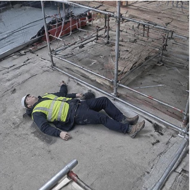 Staged person down beside construction scaffolding — synthetic demonstration, not live